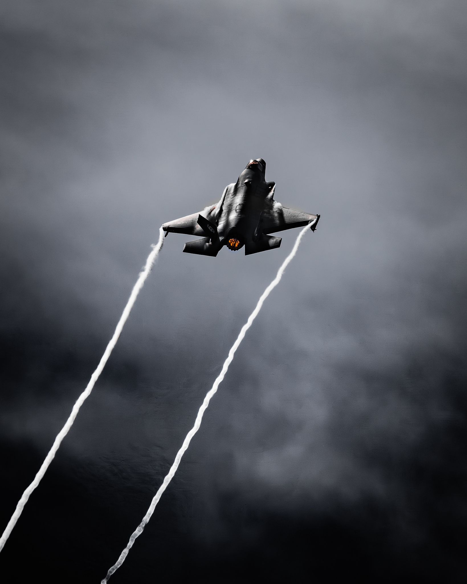 An F-35 climbing through gray sky with vapor trails.